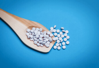 Pills from pharmaceutical medicine, on a wooden spoon, on a blue background.