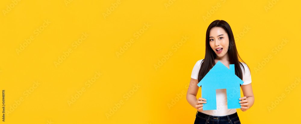 Young beautiful Asian woman holding new house model cutout isolated on colorful yellow banner background with copy space - obrazy, fototapety, plakaty 