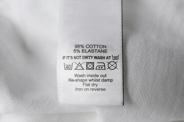 Wall Mural - Clothing label with care symbols and material content on white shirt, closeup view