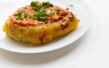 A portion of potato casserole with sauce and herbs on a white plate