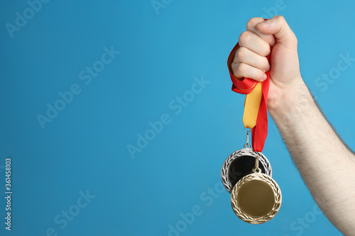 Fotografía Man holding medals on blue background, closeup. Space for design