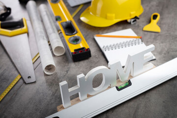 Contractor concept. Tool kit of the contractor: yellow hardhat, libella, hand saw. Plans and notebook on the gray tiles background.