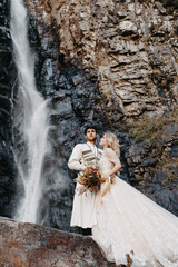 Wall Mural - noise effect, selective focus: incredibly enamored brides hugging, kissing and posing for a photo on the incredible rocky mountains background with a big waterfall