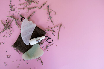 Pink and green Gua Sha massage tools made of rose quartz on the pink background with dried lavender flowers. Beauty concept. Flatlay concept 