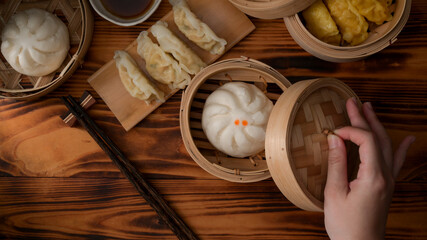 Wall Mural - Overhead shot of female hand opening bamboo seamer to eat steamed pork buns and dumplings