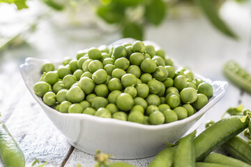 Wall Mural - Green raw peas and pods in pocelain bow isolated on wooden table