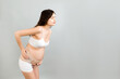 © sosiukin - Portrait of pregnant woman in underwear wearing maternity belt on her belly and showing thumb up gesture at gray background. Orthopedic abdominal support belt concept. Copy space