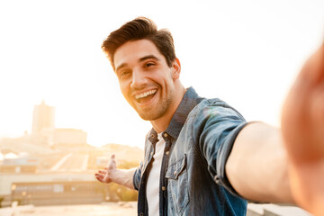 Wall Mural - Photo of joyful unshaven young man laughing while taking selfie photo