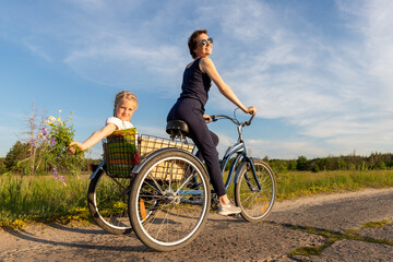 Young adult caucasian mom enjoy having leisure fun riding bicycle with cute adorable blond daughter holding wild field flower at scenic rural country road on bright sunny day. Countryside vacation