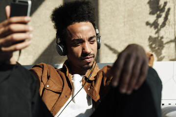 Wall Mural - Photo of focused african american man using headphones and cellphone