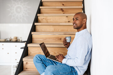 Wall Mural - Photo of man using laptop and drinking coffee while sitting on stair