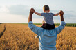 © cherryandbees - farmer holding his grandson standing in wheat field