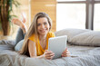 © Prostock-studio - Smiling millennial woman using tablet computer for online work or education on bed at home, blank space