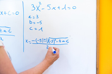 Teacher writing a math formula on a white board with a blue marker.