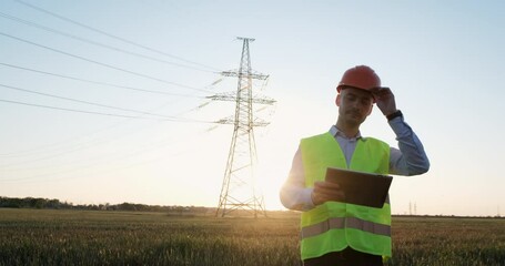 Wall Mural - a power engineer in a protective helmet and special clothes stands on the background of a high-volta