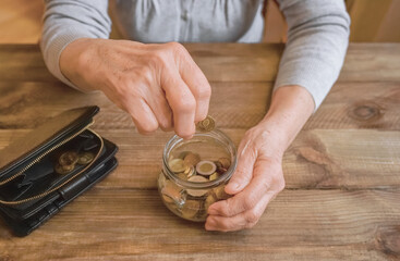 Wall Mural - Old wrinkled hand holding jar with coins, empty wallet, wooden background. Elderly woman throws a coin into a jar, counting. Saving money for future, retirement fund, pension, poorness, need concept.