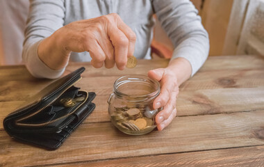 Wall Mural - Old wrinkled hand holding jar with coins, empty wallet, wooden background. Elderly woman throws a coin into a jar, counting. Saving money for future, retirement fund, pension, poorness, need concept.