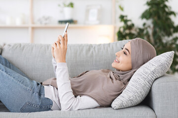 Poster - Relaxed Arabic Girl In Hijab Resting On Couch With Smartphone In Hands