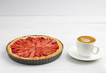 Homemade rhubarb and strawberry pie and cup of coffee on white wooden table. Angle view. Copyspace.