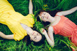 Two young girls lie in the grass in the meadow. Bright outfits and green grass