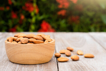 Canvas Print - Almond nuts in wooden bowl isolated on  wood table with green nature blurred background. 