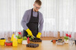 © Model Republic - young man with glasses and apron wearing yellow rubber gloves planting seedlings in pots in country house in background of white curtain Stress Management Concept