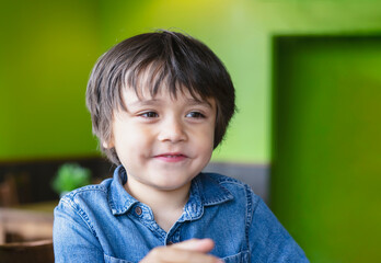 Portrait of happy little boy with smile sitting in the cafe waitting for food, Cheerful kid looking at camera with smling face, Positive childhood concept