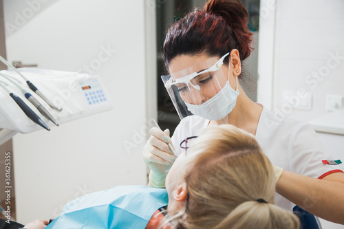 Closeup shot of dentist in protection mask working with tooth cavity and plague. Patient on stomatology chair repair aching teeth. Stomatologist and patient at clinic office. Toothcare concept