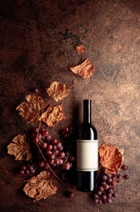 Wall Mural - Bottle of red wine with ripe grapes and dried up vine leaves. Old copper background.