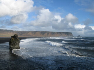 Reynisfjara - seascape with black sand beach, blue sea, blue sky and white clouds, Iceland