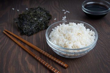 Wall Mural - Bowl of steamed white rice together with chopsticks and dry seaweed are laying on dark wooden table at kitchen