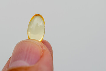 vitamin d, fingers holding capsule, white background.