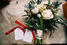 Bridal Bouquet Of Pink And White Roses, Tulips, Branches Of Eucalyptus Tree, Eryngium, Scabiosa, Silver Brooch And White Ribbons On The Floor, Cards With Red Ribbons Near It