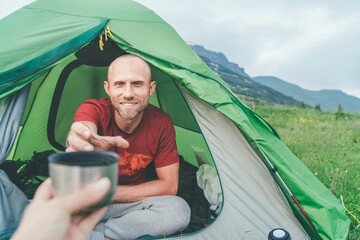 Wall Mural - smiling bald man in the green tent taking the thermos teacup for morning tea-drinking with mountain 