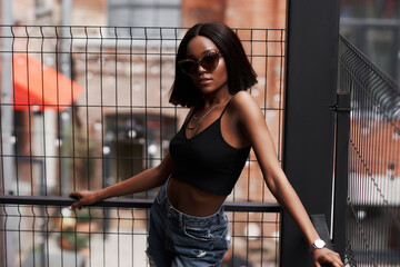 Fashion outdoor portrait at urban location. Girl wearing blue jeans, black top and sunglasses. Woman sitting and posing, Sensual fenale model