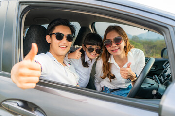 Happy Asian family with father thumb up and mother and daughter wear sunglass in compact car are smiling and driving for travel on vacation. Car insurance or rental .