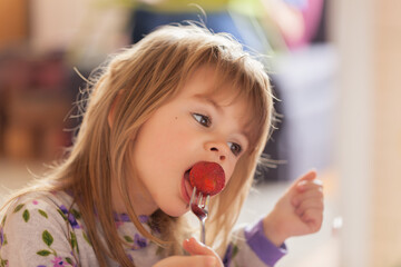 adorable little girl in pajama eating strawberries at home