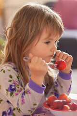 Wall Mural - Adorable little girl in pajama eating strawberries at home