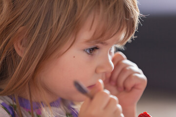 Wall Mural - Adorable little girl in pajama eating strawberries at home