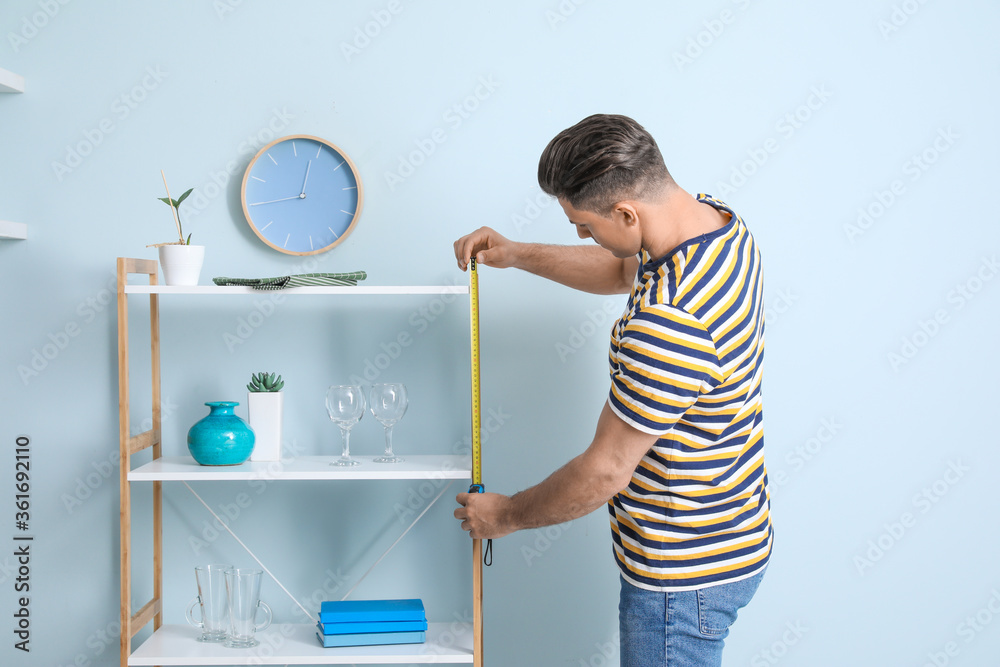 Young man taking measures of rack in room