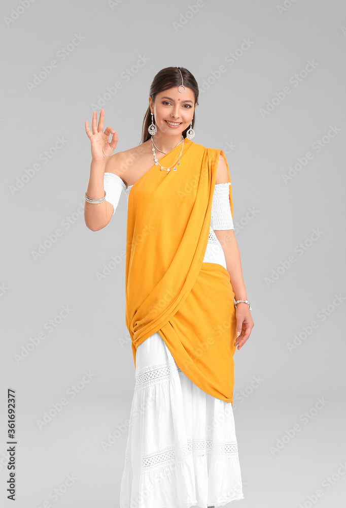 Beautiful young Indian woman showing OK on grey background