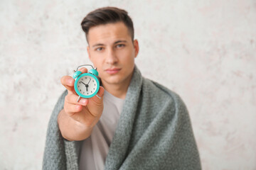 Tired man with alarm clock and plaid on light background. Concept of sleep deprivation