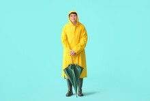 Young Asian Man In Raincoat And With Umbrella On Color Background