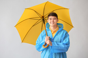 Wall Mural - Young Asian man in raincoat and with umbrella on grey background