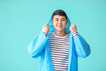 Wall Mural - Young Asian man in raincoat on color background