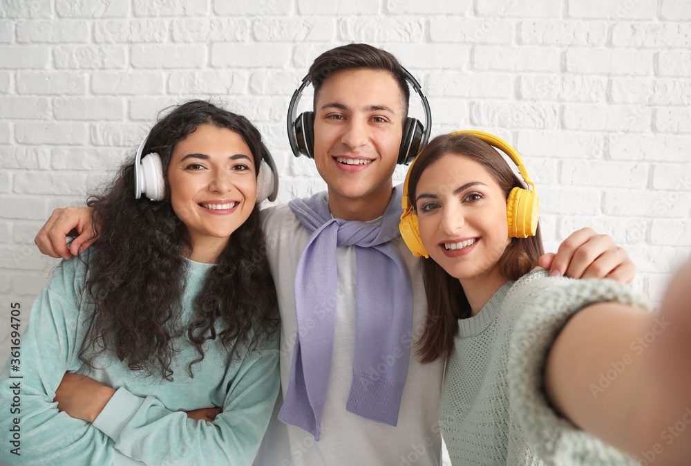Young friends taking selfie on white brick background