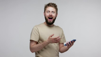 Wall Mural - excited amazed bearded man looking at camera with big eyes surprised expression after using mobile p