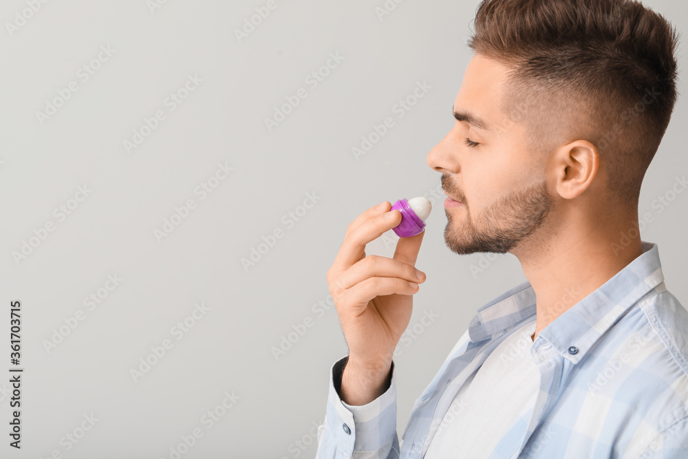 Handsome young man with lip balm on light background