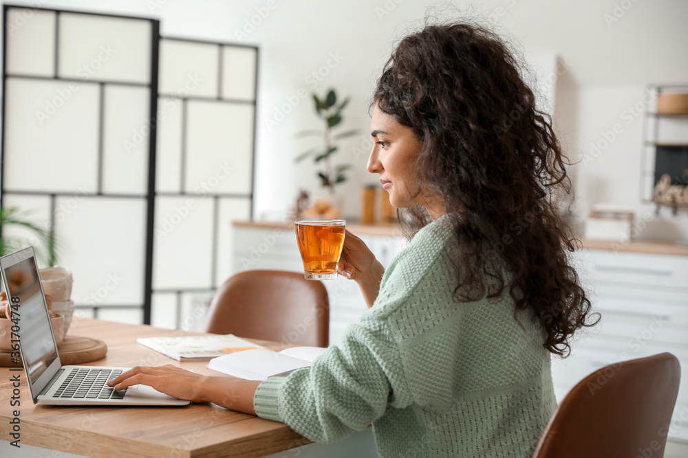Beautiful young woman drinking hot tea while working at home