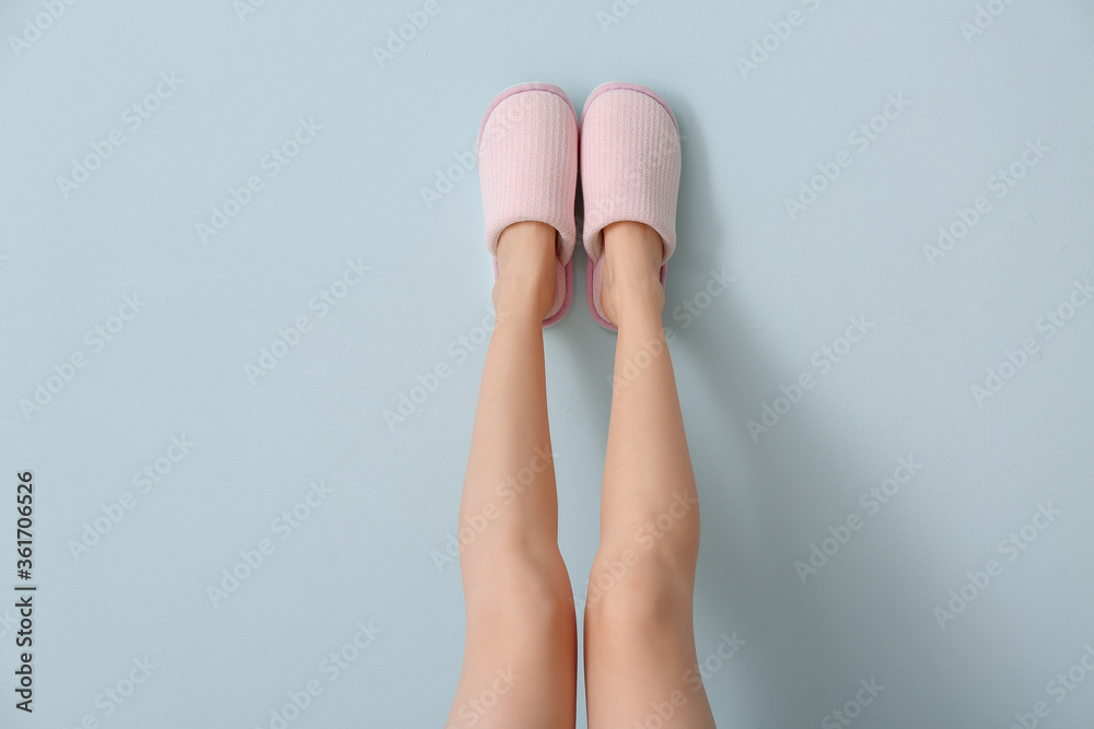 Female legs in soft slippers on color background